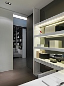 Modern shelves with integrated lighting in front of a gray wall in a home office with open hallway and view into a living room