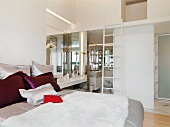 Farbige Kissen auf Doppelbett in modernem Schlafzimmer mit Blick ins Bad ensuite