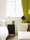 White bedroom with a chaise lounge and green curtain