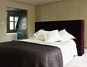 Doppelbett mit gepolstertem Kopfteil und violettem Bezug vor Wandschrank in modernem Schlafzimmer mit Bad ensuite