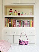 Bed in front of fitted cabinet with shelves and handbag hanging from drawer handle