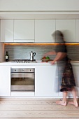 Modern kitchen - woman standing in front of kitchen units with white wall units and base units