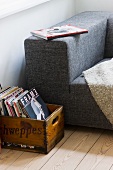 Vintage wooden crate of books next to partially visible modern couch with mottled grey fabric cover