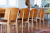Simple, modern wooden chairs around dining table on colourful rug