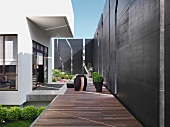 Asiatisch schlichter Gartenbereich eines modernen Wohnhauses mit hohen, geschlitzten Sichtschutzwänden entlang eines Holzdecks