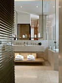 Beleuchtete Handtuchablage unter Doppelwaschbecken und Hängeregal vor dem Spiegel im modernen Bad mit Natursteinfliesen