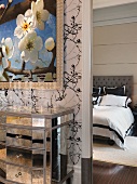 Spiegelkommode unter stilisiertem Kirschblütengemälde und Blick auf das schwarzweiss bezogene Doppelbett