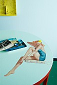 Round table top with photorealistic, fifties-style painting of woman in bathing suit sitting on diving board