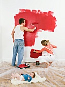Couple painting a wall, baby on floor