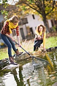 Zwei junge Frauen reinigen Gartenteich mit Rechen