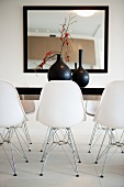 Detail of dining room with large, framed mirror on wall, black table and white designer shell chairs