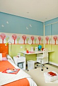 Pastel colors in a child's bedroom - stenciled wall behind a work station in neutral white and orange linens on the bed
