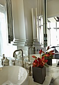 Ausschnitt des Waschtisches und Spiegels eines elegant-modernen Badezimmers mit rotschwarzer Blumendeko