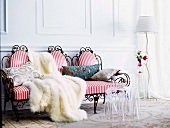 Romantic seating area with draped fur blanket on red and white striped upholstery of delicate, antique-style wire bench