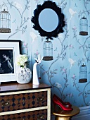 Hand ornament as jewellery stand on vintage chest of drawers against romantic wallpaper with birdcage motif