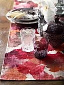Vintage glasses and sugar bowl next to place setting on table runner with red, batik-effect pattern of leaves
