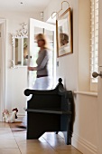 Black armchair in white hallway with woman coming in through front door