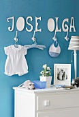 Babyzimmer mit blauer Wand und daraufgeklebten Namen aus Pappe über weissen Kleiderhaken