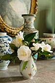 Posy of white roses in china vase in front of collection of vases and gilt-framed picture