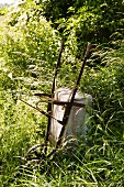 Antique wheelbarrow tipped on end in long grass of sunny meadow