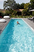 Man swimming in narrow pool on sunny wooden terrace with various seating