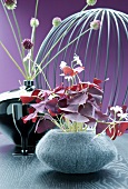 Gray felt vase with red clover in front of a ceramic vase with allium