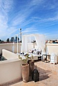 Blue sky above Oriental roof terrace with planters and modern, canopied daybed on terracotta floor