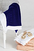 Blue blanket on white wicker chair next to white flip-flops on basketwork chair cushions