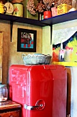 Red, retro fridge under small paintings and colourful pots on simple wooden shelf in corner of kitchen