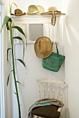 Several straw hats on white coat rack above white vintage chairs and freshly-cut stem of giant cane