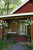 View into roofed entrance area of Scandinavian wooden cabin with bench and antlers on wooden wall