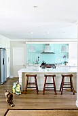 Bright country-house kitchen with pastel turquoise back wall and rustic wooden stools at breakfast bar