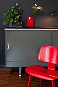 Red classic chair in front of grey designer sideboard against black wall