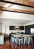 Offene Küche in großzügigem Dachraum mit Metallhockern an ausladendem Tischblock mit Steinplatte