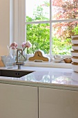 Modern kitchen unit with white countertop in front of a window with a view of the garden