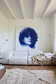 Living room with a white rug and couch upholstered in light fabric in front of a wall with a portrait drawing