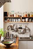 Dried ingredients on open shelving and utensils hanging from a pan rack in kitchen corner with sinks and solid oak work surfaces