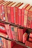 A wooden shelf with three rows of vintage red books
