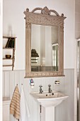 Nostalgischer Badezimmerspiegel mit dekorativem, grau lackierten Holzrahmen über antikem Standwaschbecken
