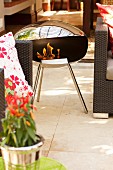Portable, stainless steel fire bowl flanked by terrace furniture on veranda
