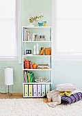 Books and box files on modern shelves against pastel blue wall and stack of cushions on flokati rug