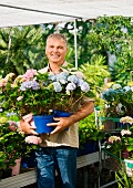 Älterer Mann steht mit Topfblumen in einem Gartencenter