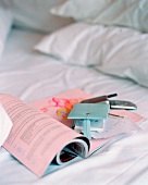 Zeitschrift, Notizbuch und Mobiltelefon auf einem Bett