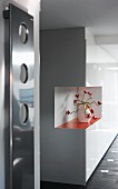White, glossy, fitted cupboards with cut-out corner and orange shelf holding crocheted, floral ornament