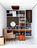 Smart fitted shelving in reading corner with traditional wing-backed chair and foot stool combined with pretty designer lamp