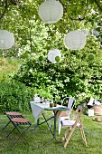 Set table with bench and rustic chairs below lanterns hanging from tree in garden