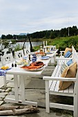 Festively set garden table with robust, white, country-house-style wooden furniture on lakeside terrace