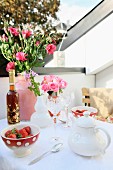 Bouquets of lisianthus and roses in Moroccan ceramic vases decorating table on roof terrace set with dishes of strawberries and crystal glasses