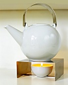 Lit candle under teapot on metal stand