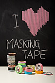 Bunte Masking-Tape-Rollen vor Tafel mit Herz-Motiv und Schriftzug